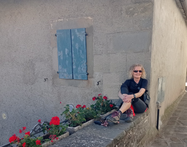 Rosa Pellegrino, scrittrice di scienze del web e specialista SEO, seduta su un muro di pietra accanto a una finestra chiusa con persiane blu e decorazioni di fiori rossi.